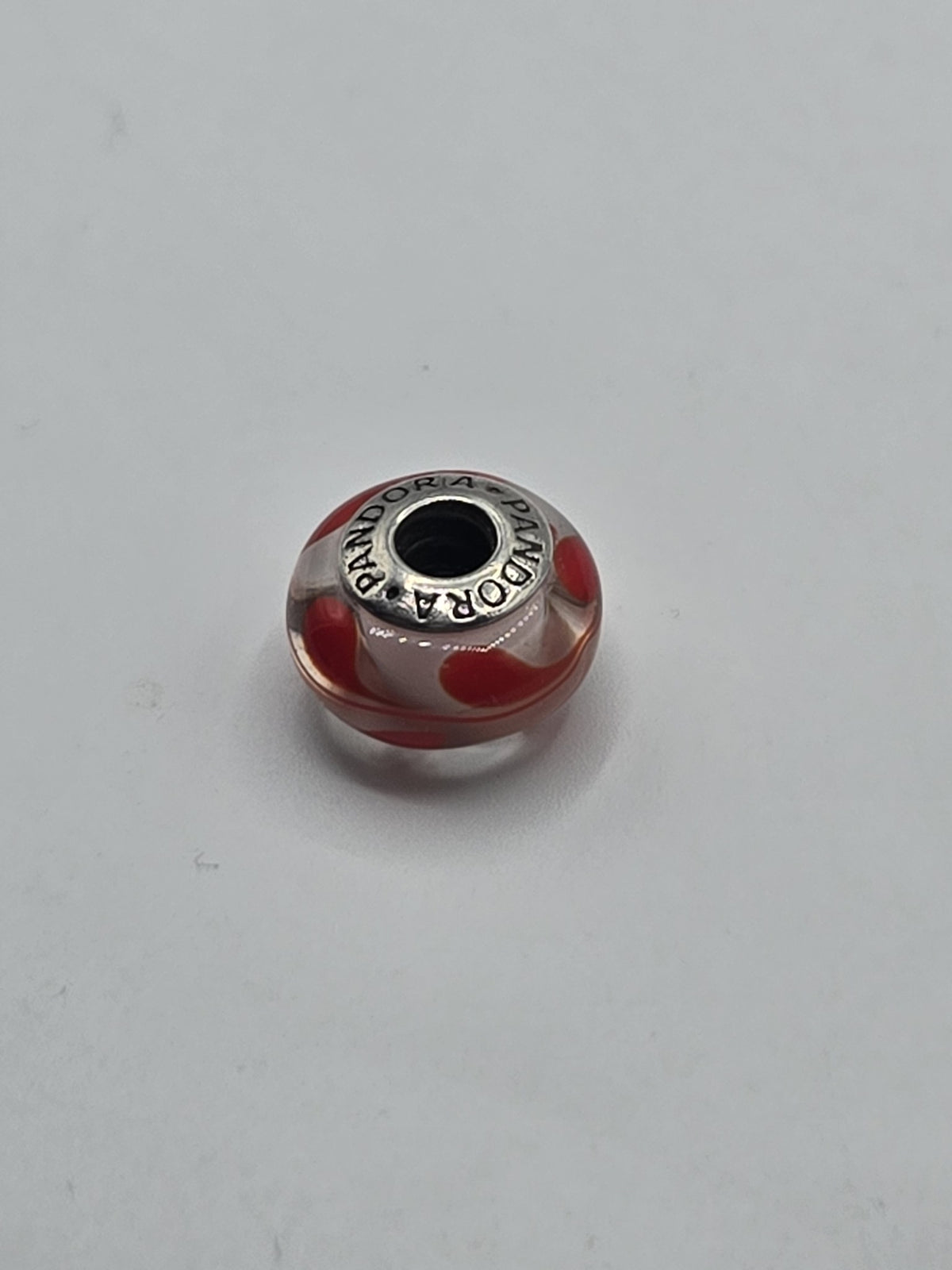 Pandora Clear and Red Heart Swirl Murano Glass Charm on a plain light background